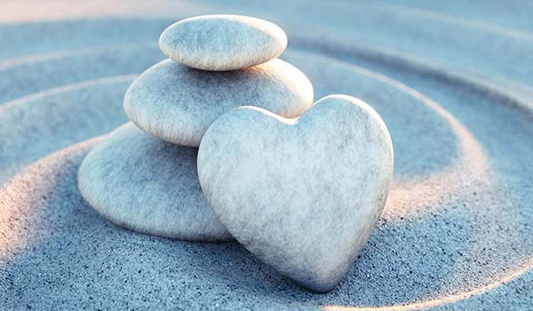Three smooth stones, two stacked and one heart-shaped, rest on raked sand with circular patterns.