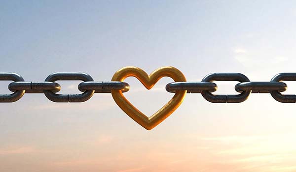 A metal chain with a gold heart-shaped link in the center, set against a sky at dusk.